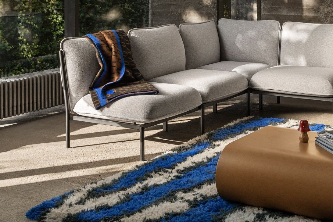 A living room scene featuring Kumo Sofa in Porcelain, Arch Throw Black / Brown / Blue, Monster Rug Ultramarine / Off-White, and Stump Coffee Table Medium Natural.