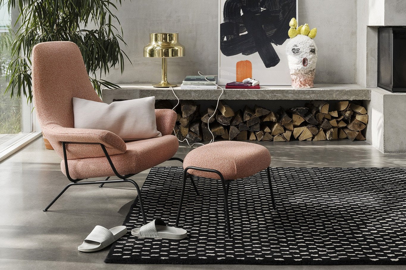 A living room setting featuring the Hai Lounge Chair + Ottoman in the shade Coral Melange / Black PC Metal, a Rain Rug and a Neo Cushion Large in the shade Shell.