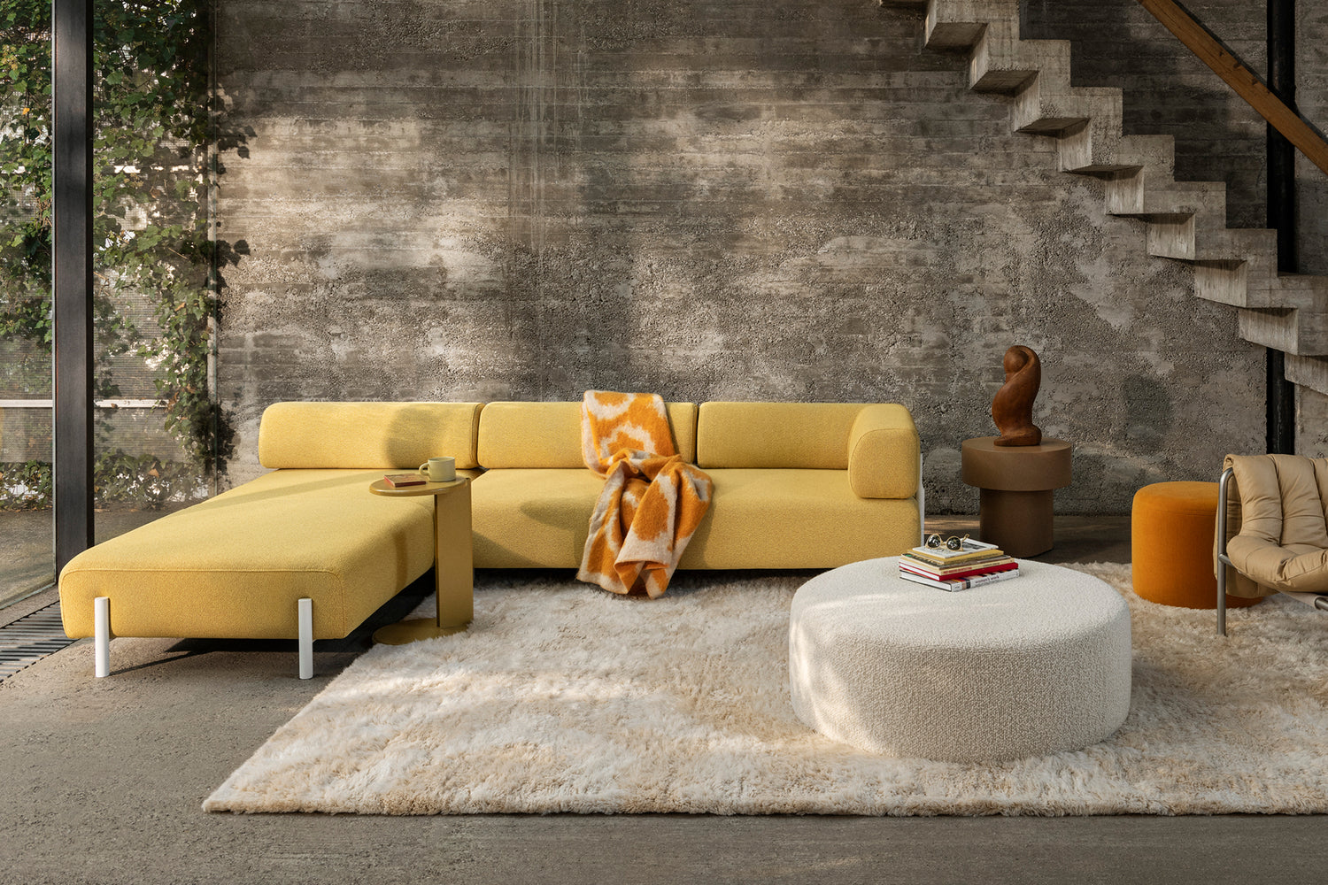 A living room scene featuring Palo Modular Corner Sofa Left in Sunflower, Monster Rug Beige / Off-White, Lolly Side Table Ochre Yellow, Monster Throw, Bon Pouf Round Large Eggshell, Stump Side Table Natural, Bon Pouf Round Ochre, and a Puffy Lounge Chair.