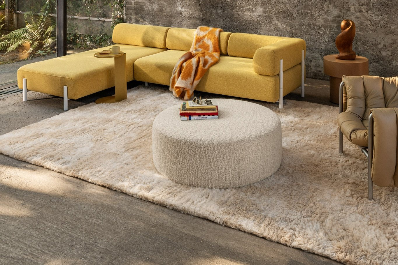 A living room scene featuring Palo Modular Corner Soft Left Sunflower, Lolly Side Table Ochre Yellow, Monster Throw Ochre / Off-White Ring, Monster Rug Beige / Off-White, Bon Pouf Round Large Eggshell, Stump Side Table Natural, and a Puffy Lounge Chair.