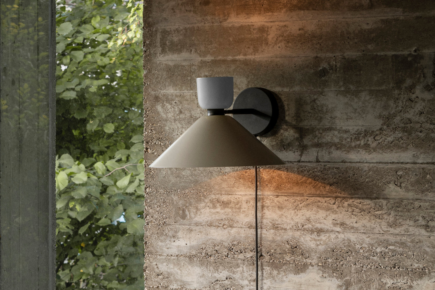 An image showing the Alphabeta Wall Light + Cable lit and mounted on a gray stone wall.