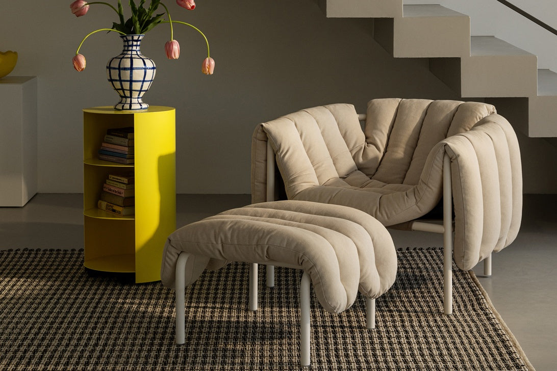 A living room / lounge scene featuring a Hide Pedestal in Sulfur Yellow next to a Puffy Lounge Chair + Ottoman in Natural / Cream PC on top of a Rope Rug.