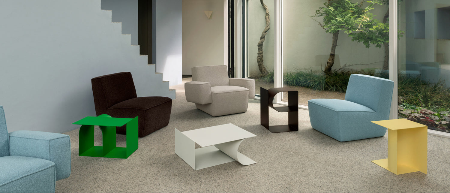 A lifestyle image of a lounge scene featuring Hunk Lounge Chair and Hunk Lounge Chair with Armrests amongst Glyph Side Tables Alpha, Beta and Gamma.