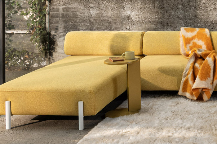 A lifestyle image of a living room scene featuring Palo Modular Corner Sofa Left Sunflower, Lolly Side Table Ochre Yellow, Monster Rug and Monster Throw.