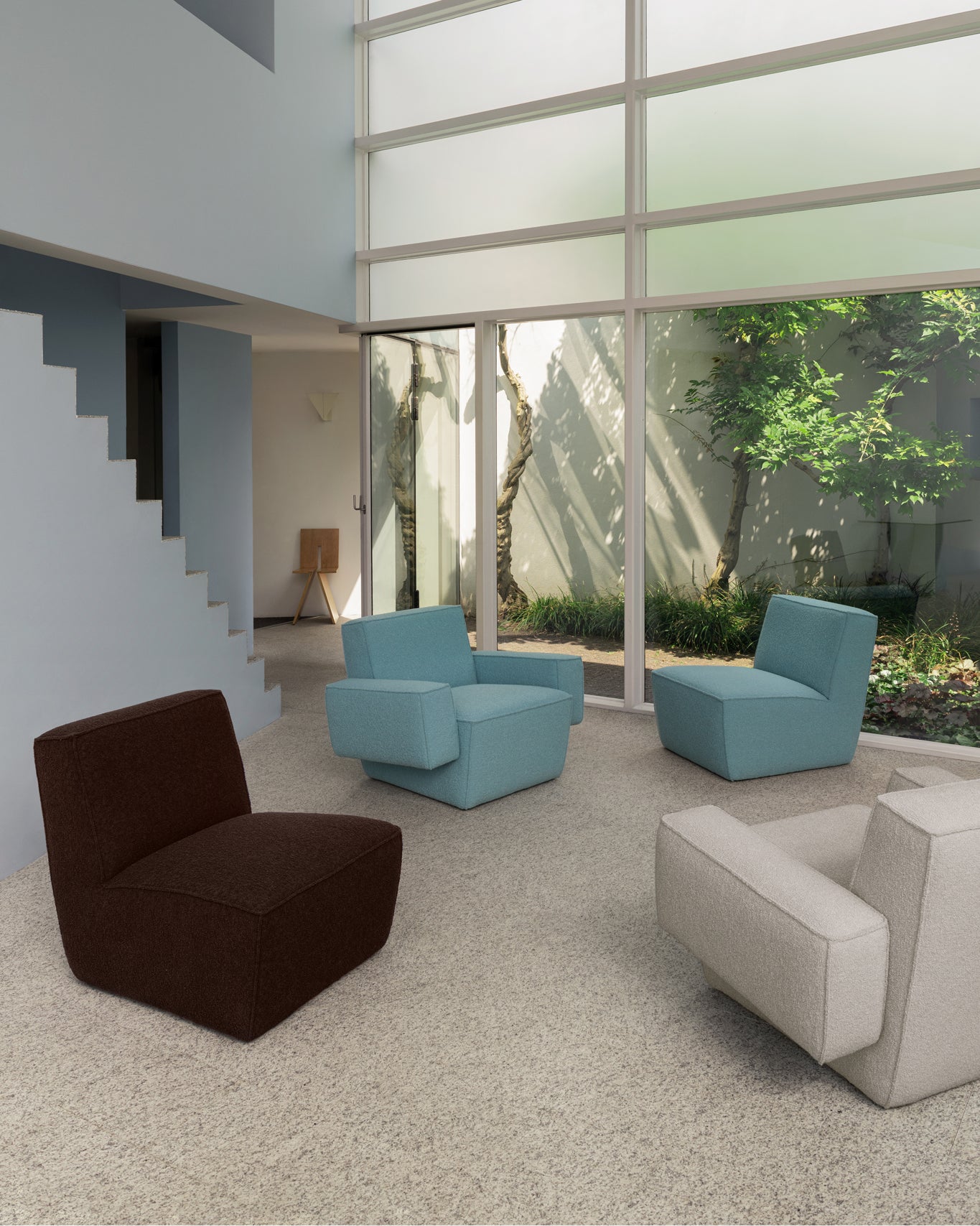 A lifestyle image of a lounge scene featuring Hunk Lounge Chair and Hunk Lounge Chair with Armrests in the shades Icicle, Chocolate Brown, and Swan.