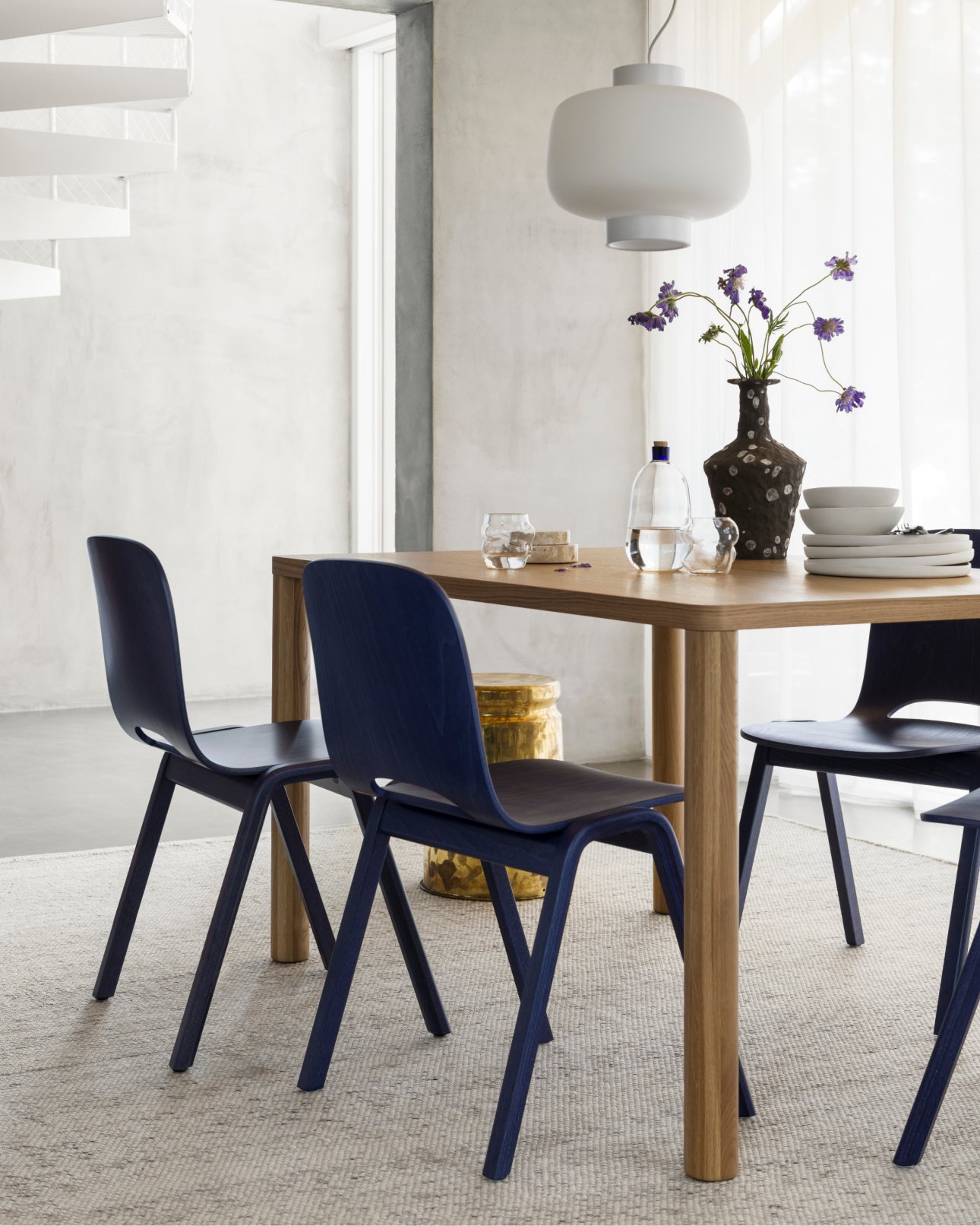 A dining room scene featuring Log Table, Touchwood Chairs in Blue, Dusk Lamp, and a Dune Rug.