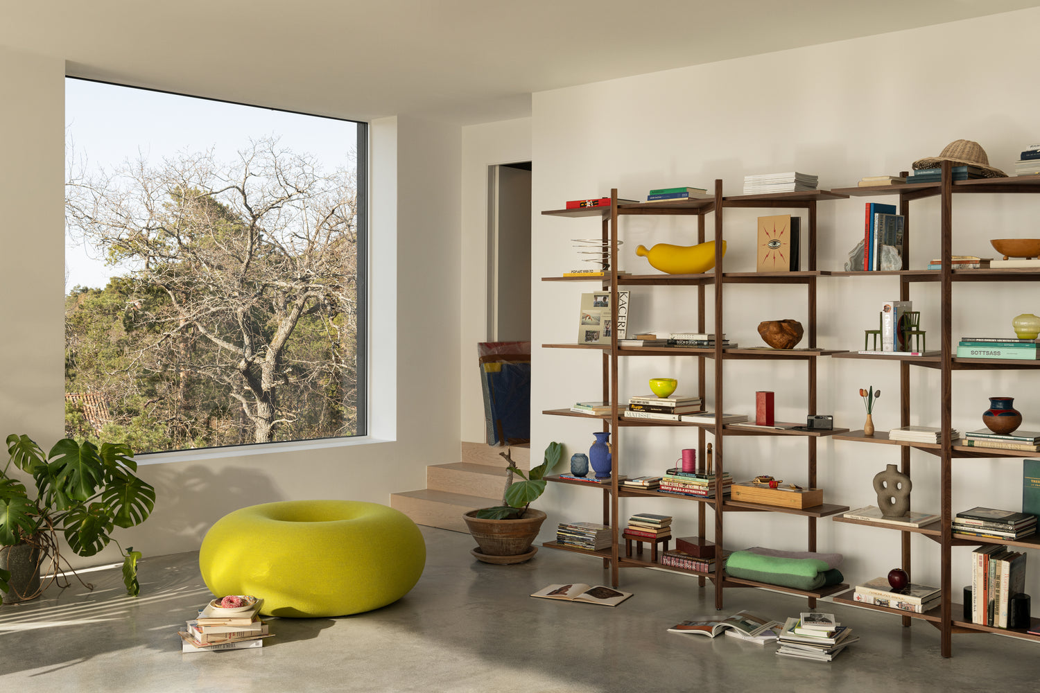 A living room / lounge scene featuring 2 Zig Zag High Shelves in the shade Walnut filled with books and other decorative objects. On the floor beside them is Boa Pouf in Sulfur Yellow.